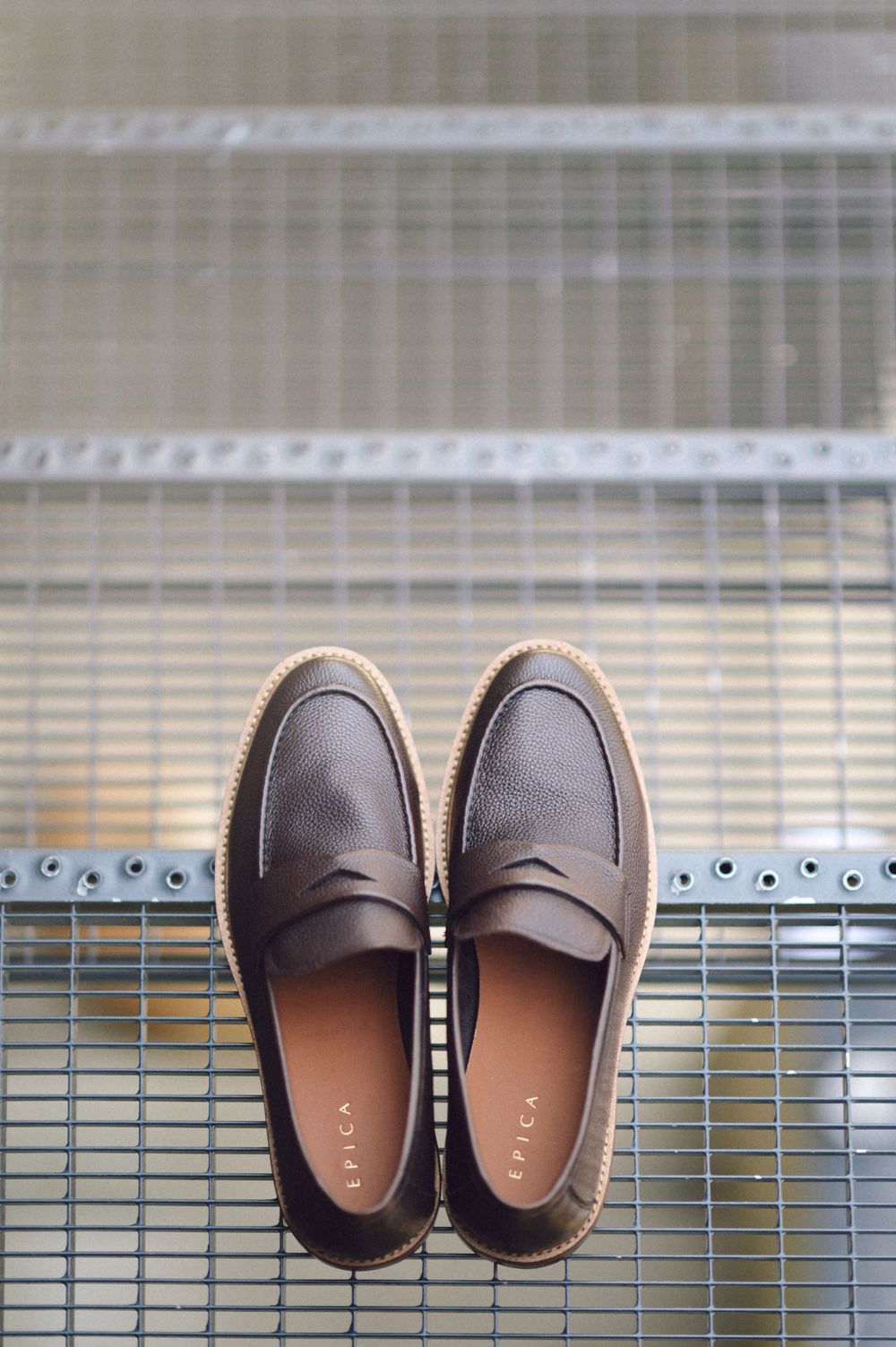 Brown leather penny loafers photographed on a metal grate surface.