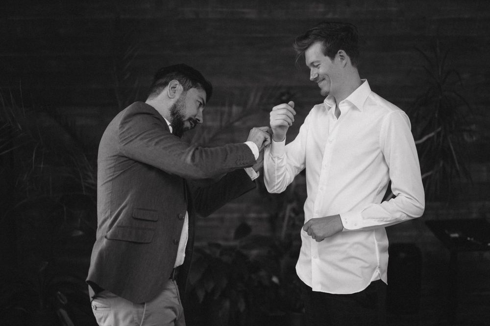 Two men in formal attire sharing a lighthearted moment in black and white photography.