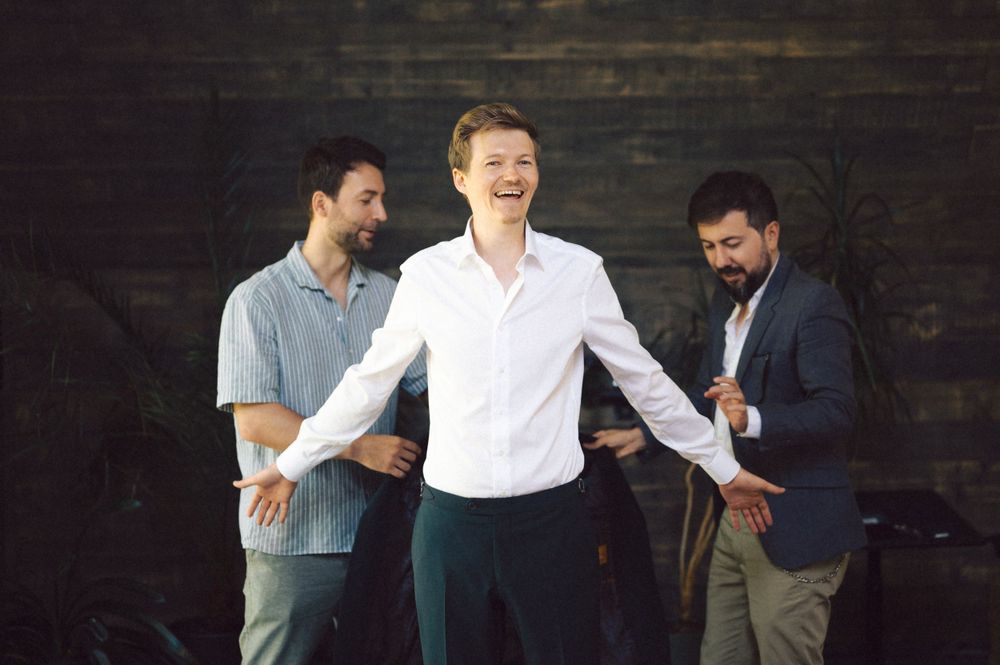 Three people helping with formal attire adjustments against a dark backdrop.