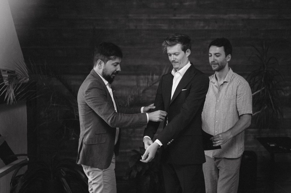 Black and white image of three people during formal wear preparations.