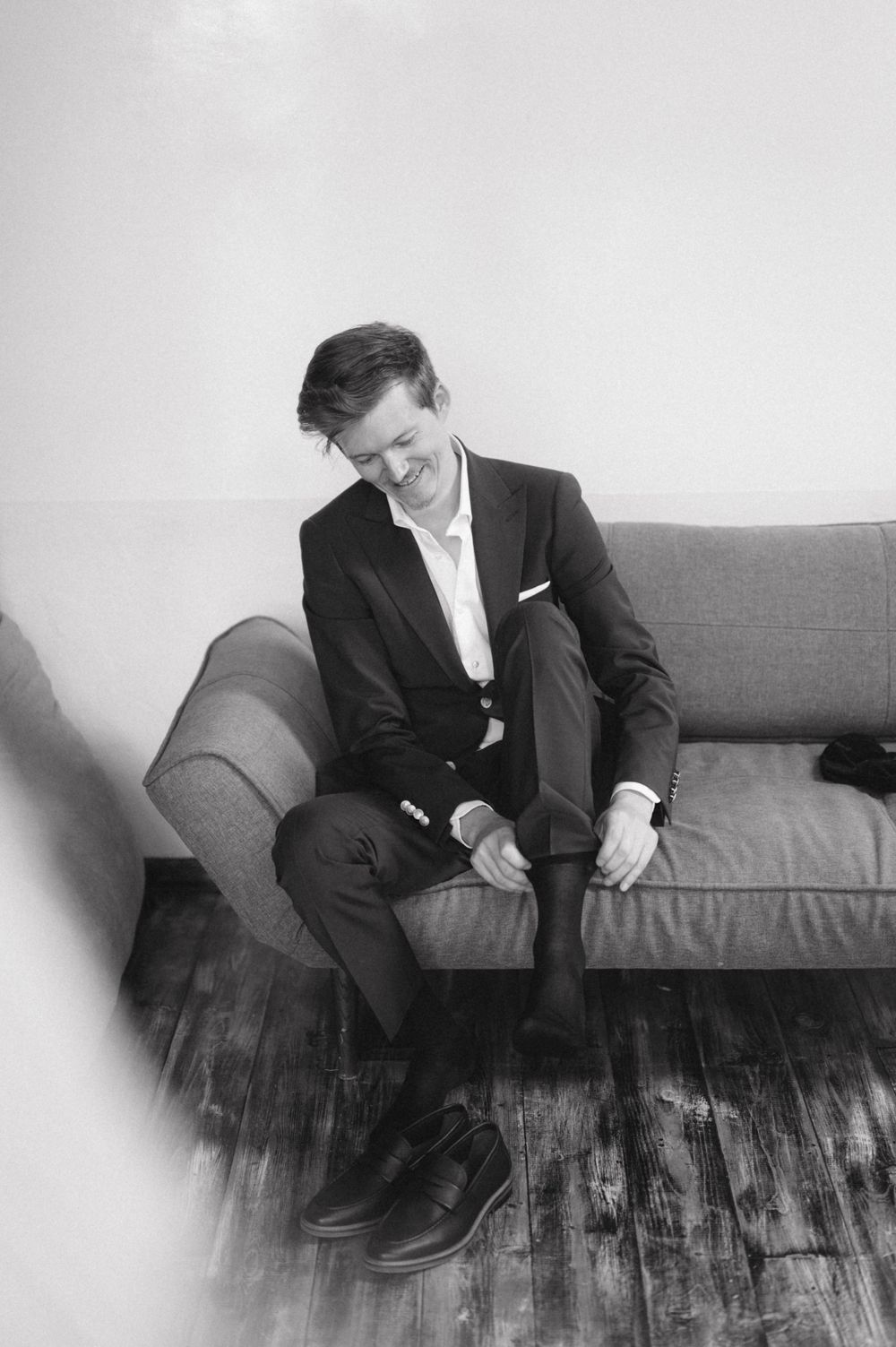 Black and white portrait of someone seated on a gray couch wearing a formal suit.