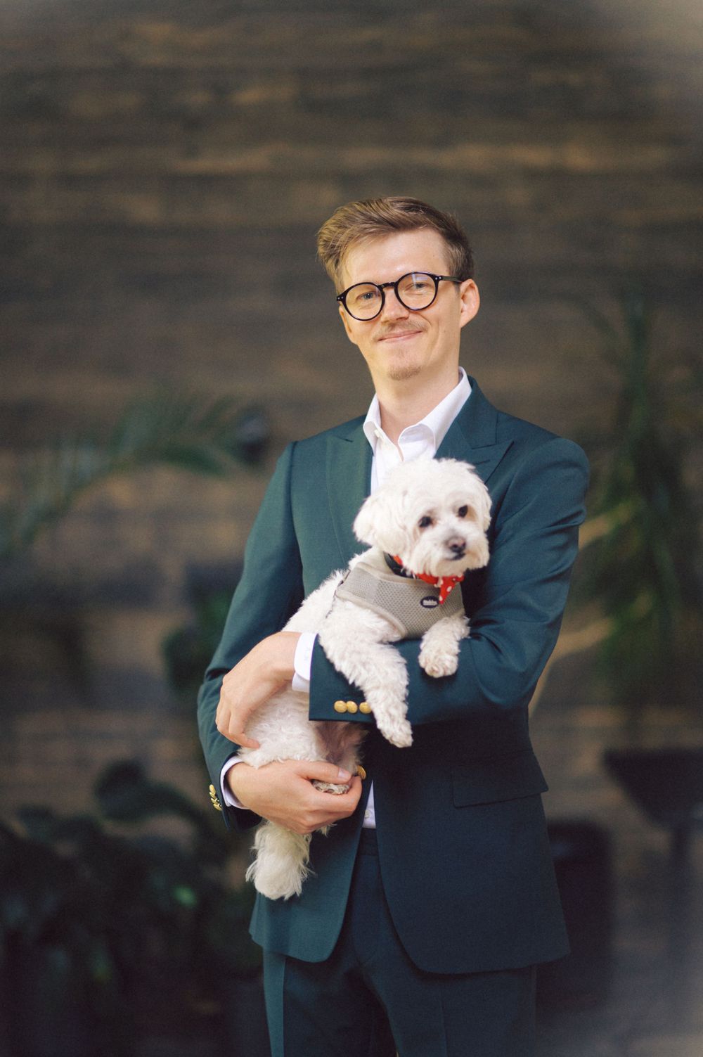 Person in navy suit holding a small white fluffy dog against wooden wall background.