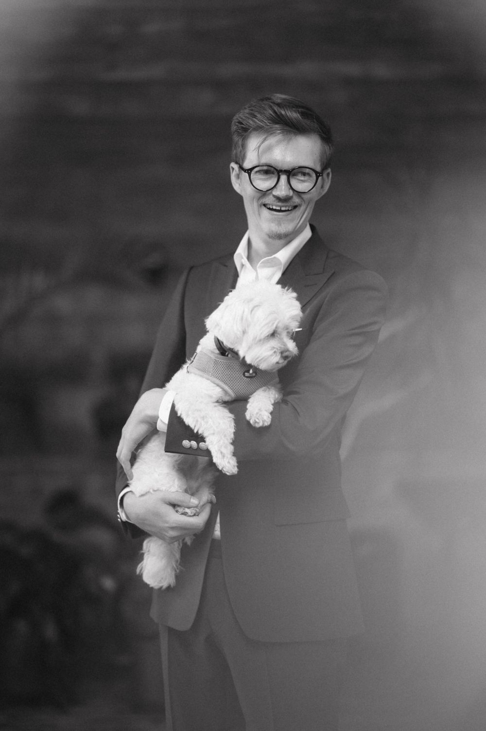 Black and white portrait of someone in a suit holding a small white dog.