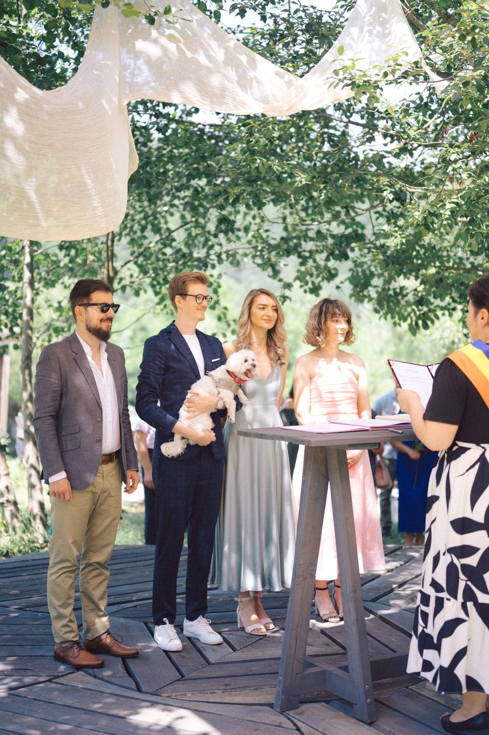 Outdoor ceremony under white fabric canopy with small dog among gathered guests.
