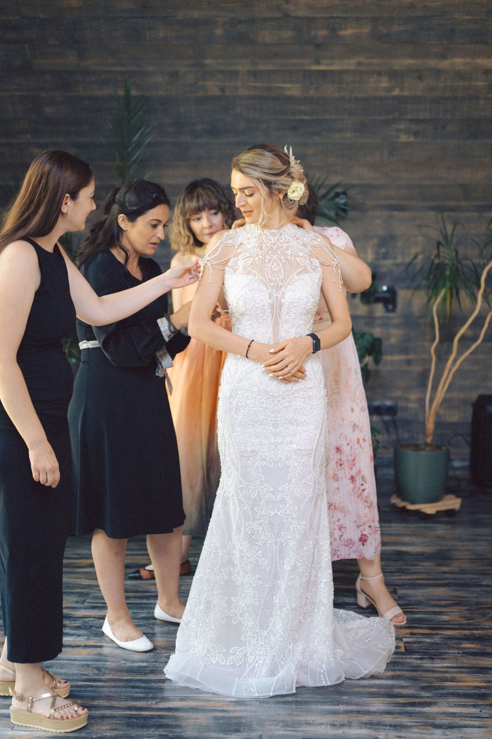 Wedding preparation scene with people gathered around a bride in an elegant lace gown.
