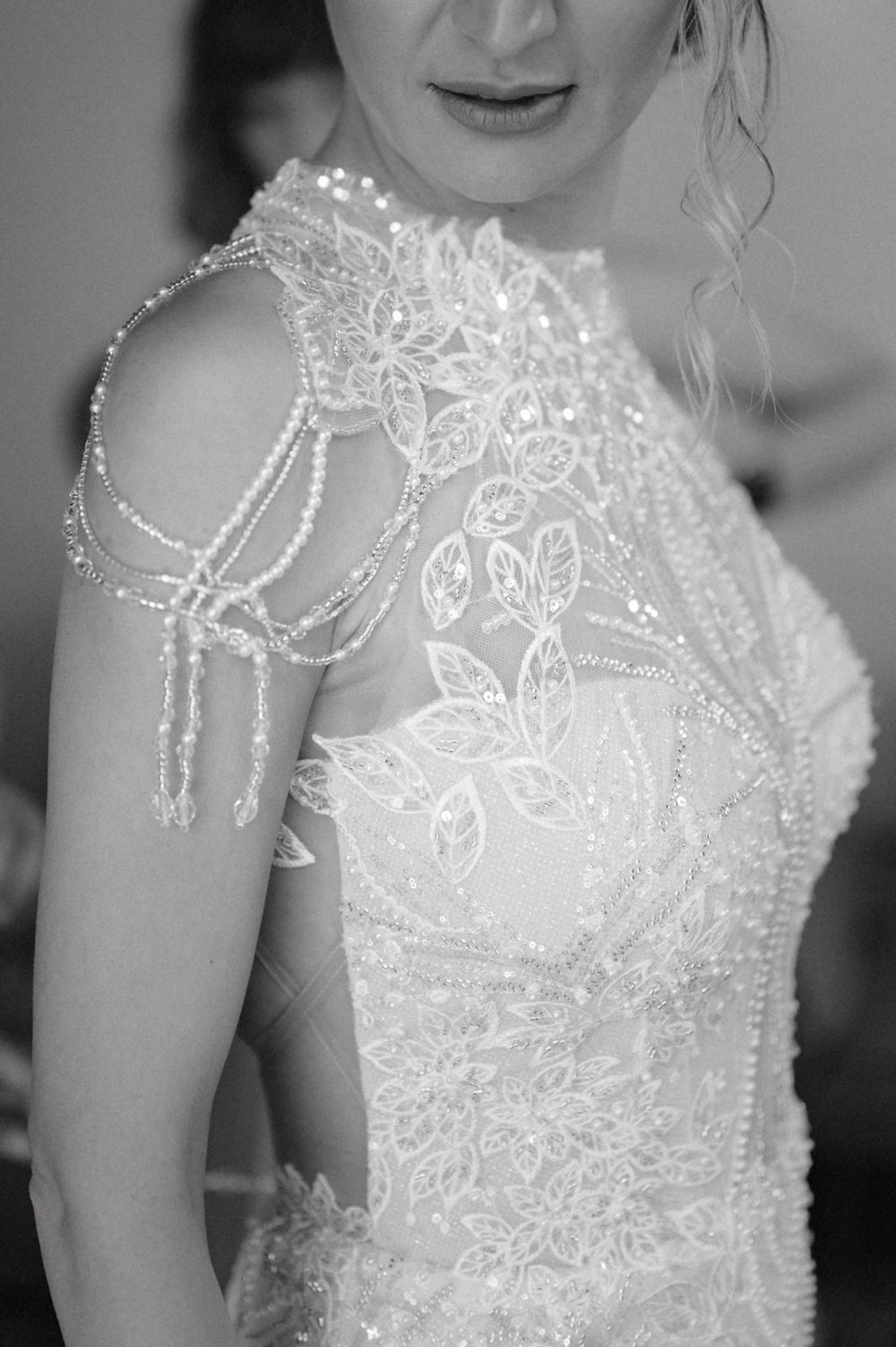 Intricate beaded detail of a wedding dress shoulder featuring delicate lace patterns.