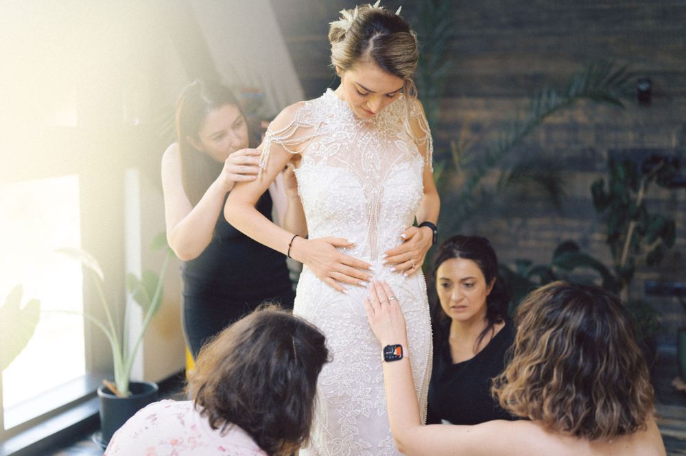Wedding dress fitting session with attendants making final adjustments in natural light.