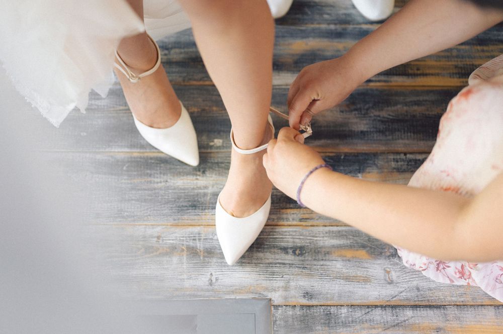 White bridal shoes with ankle straps being secured on wooden flooring.