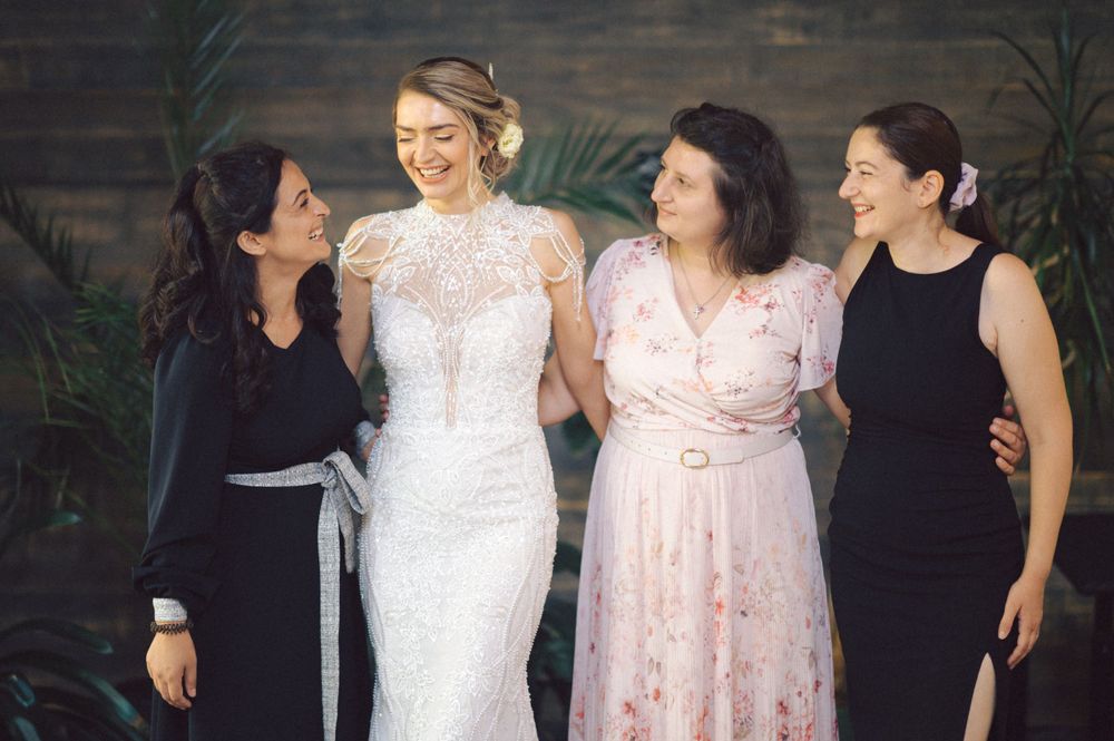 Four wedding party members share a joyful moment, with a bride in white lace and bridesmaids in black and pink dresses.