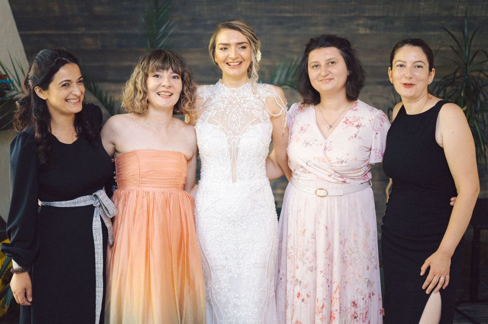 Wedding party poses together showing off their coordinated dresses in black, peach, and white against a stone wall.