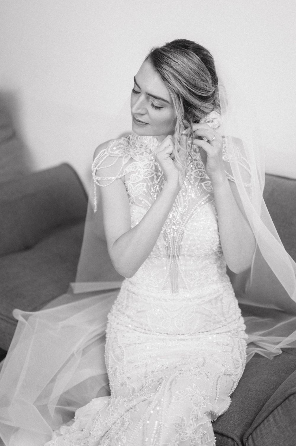Black and white portrait of a bride in a lace dress adjusting her jewelry.
