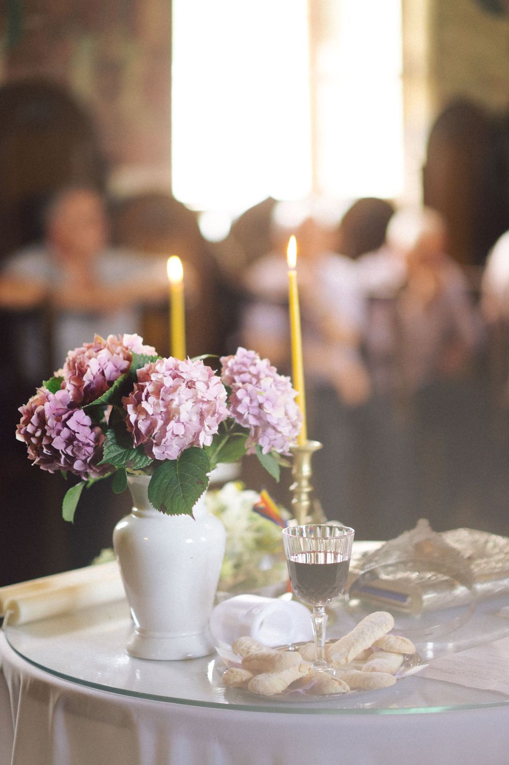 Elegant table setting with pink hydrangeas in a white vase and lit candles for a wedding reception.