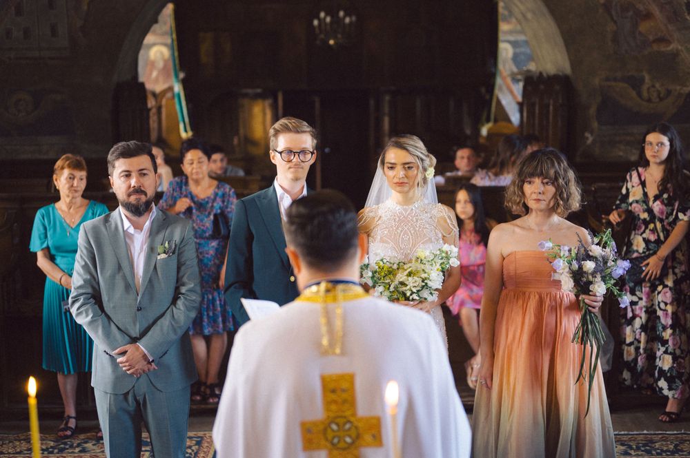 Orthodox wedding ceremony with guests gathered in a historic church with painted walls and arches.