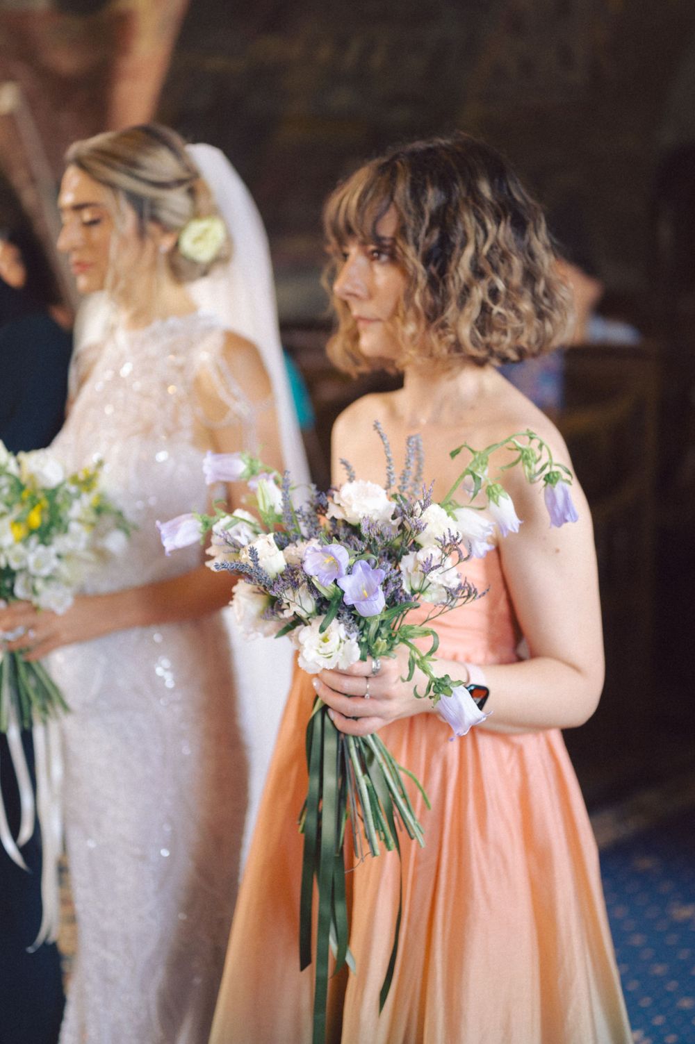 Wedding party members hold elegant bouquets during ceremony in traditional church setting.