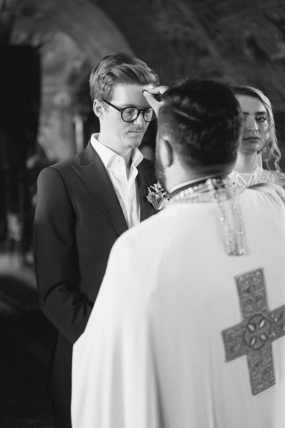 Black and white photograph of wedding ceremony conducted by Orthodox priest in traditional robes.