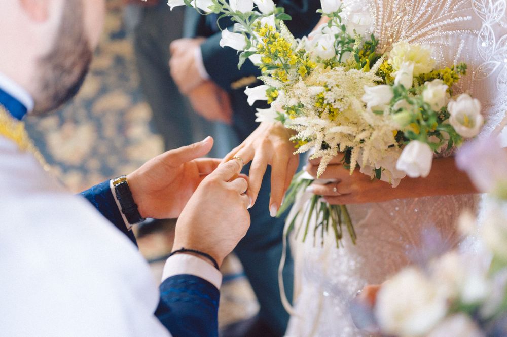 Close-up shot of hands holding a wedding bouquet during ring exchange ceremony.
