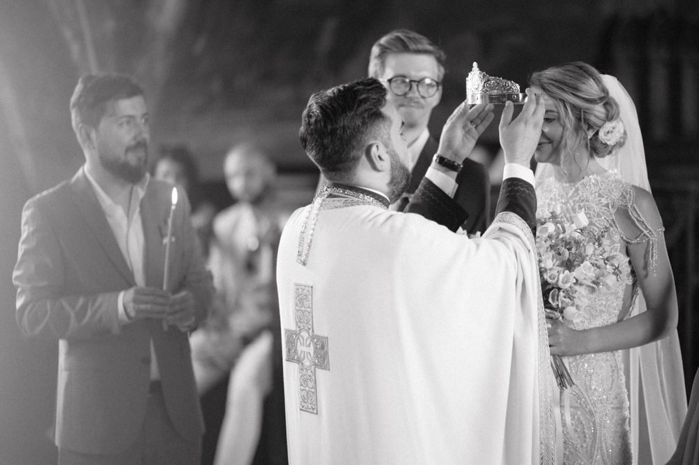 A black and white photo captures a solemn moment during an Orthodox wedding blessing.