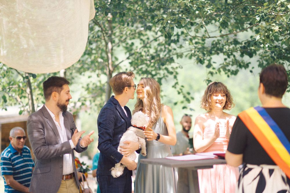 People celebrate at an outdoor gathering with paper lantern decorations and leafy tree backdrop.