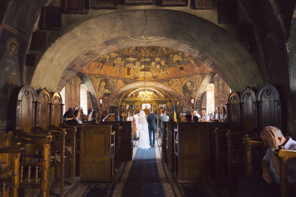 Wedding ceremony taking place in an orthodox church with beautiful painted frescoes and wooden pews.