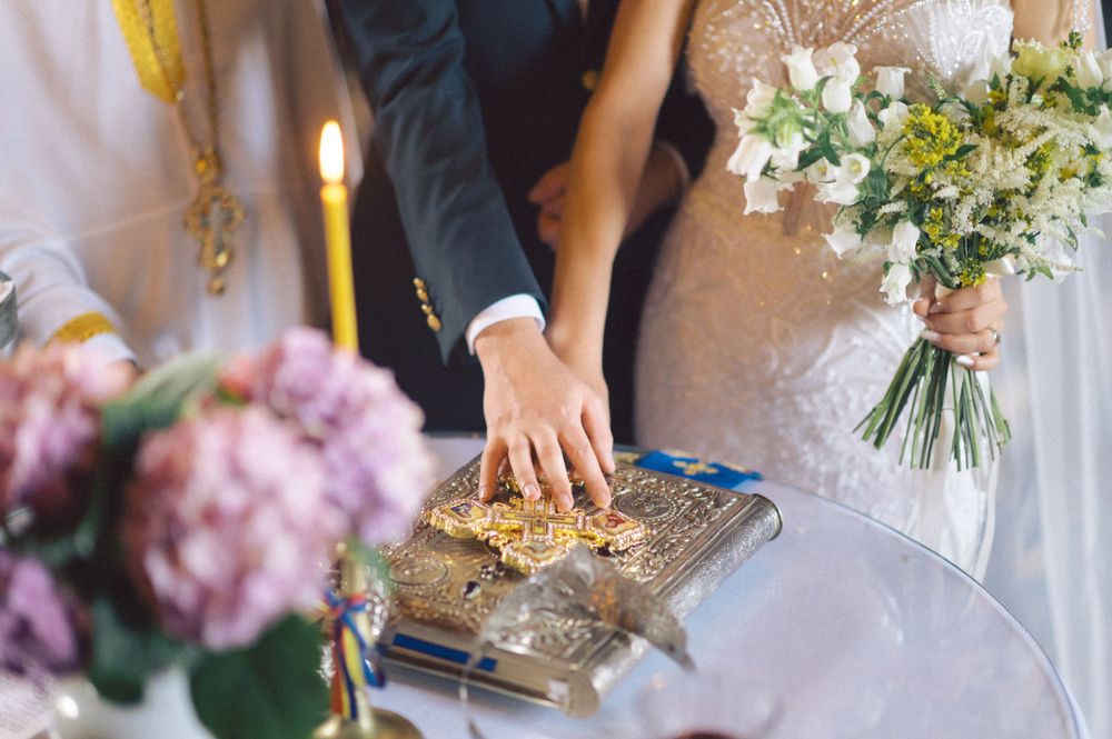 Wedding ceremony detail showing hands placing rings on an ornate holy book with flowers nearby.