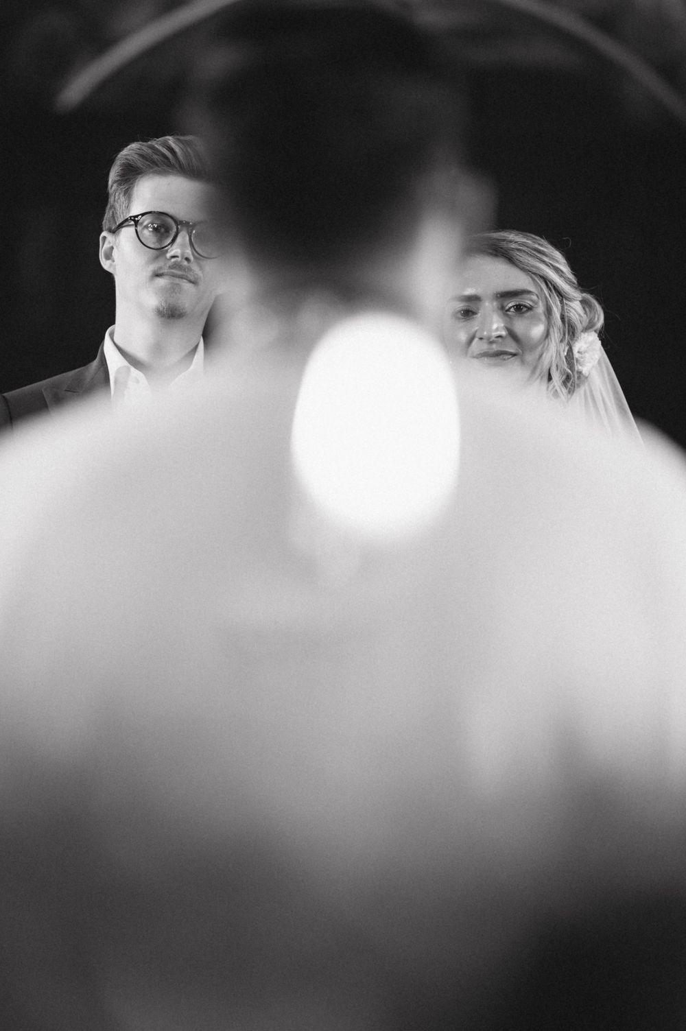 Artistic black and white wedding photo with soft bokeh effect in foreground.