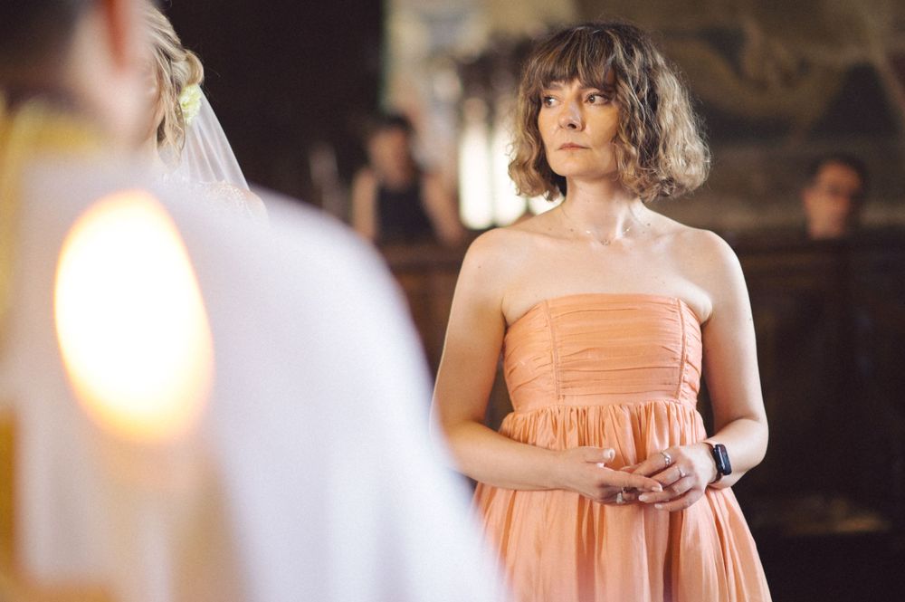 Guest in peach-colored dress watching wedding ceremony in historic church setting.