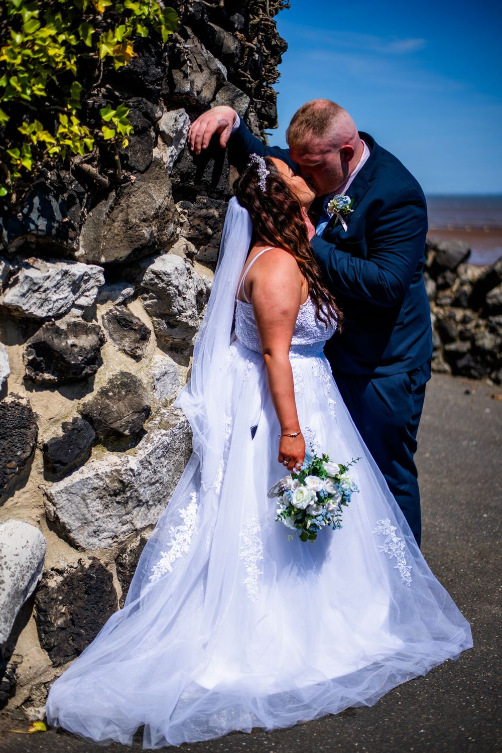 A romantic wedding photo against stone wall with ocean view.