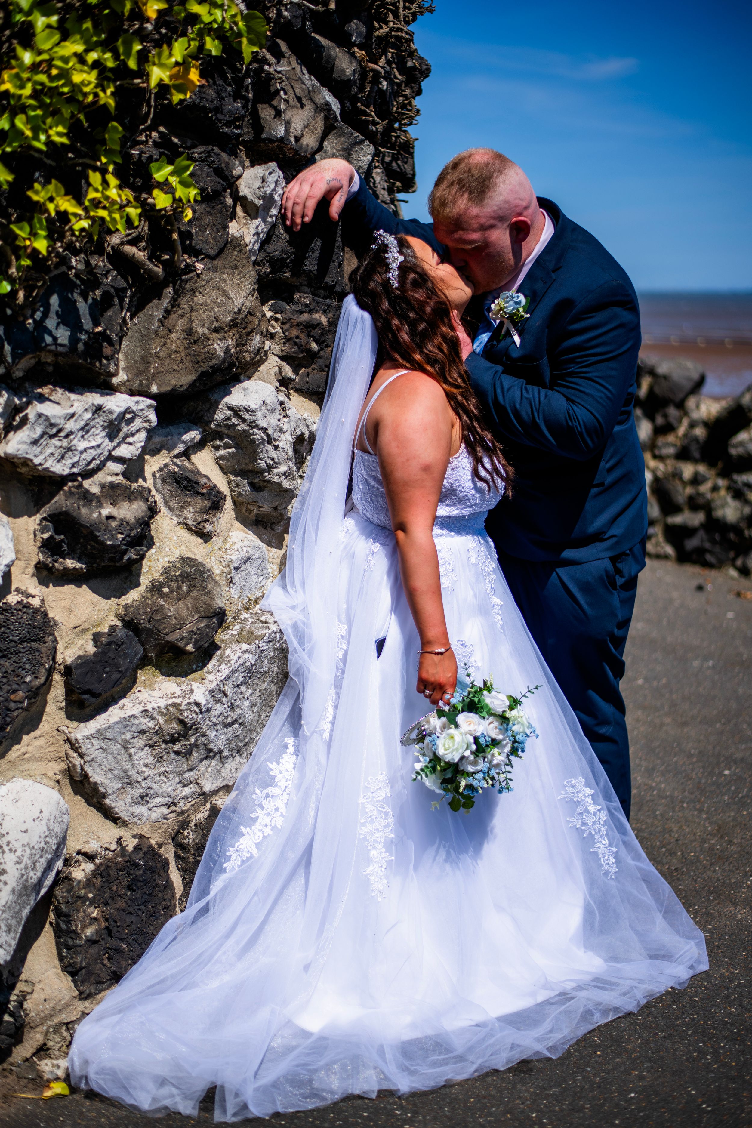 A romantic wedding photo against stone wall with ocean view.