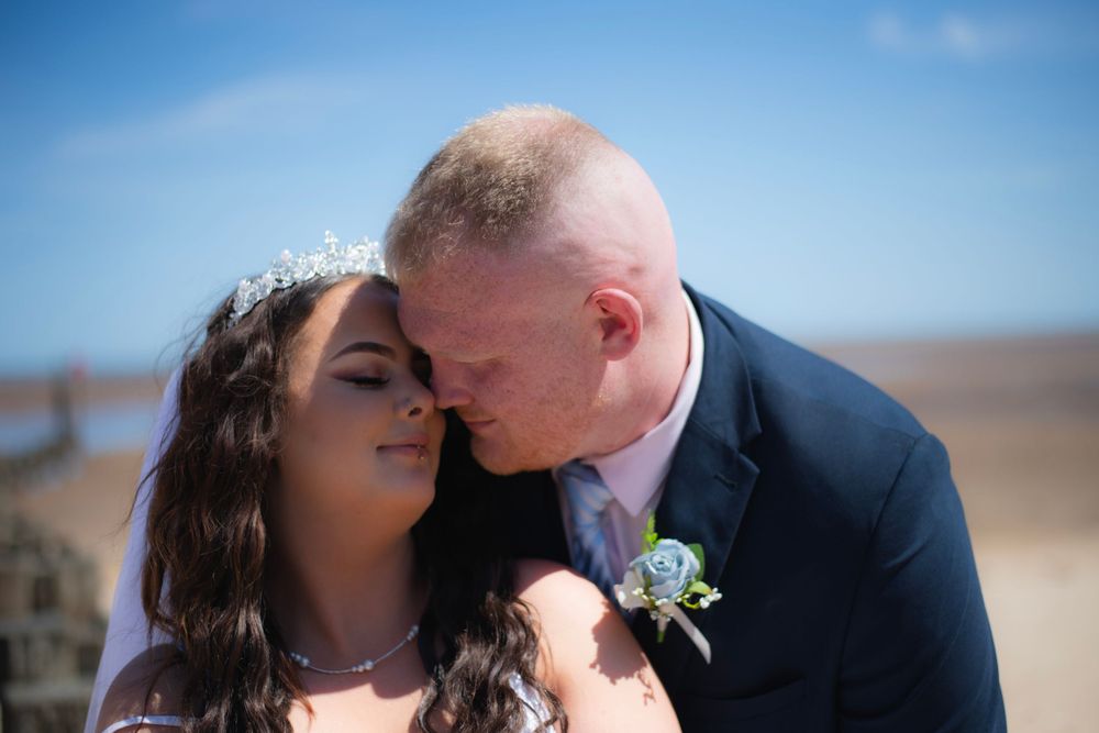 A tender moment between newlyweds on a sunny beach, with a delicate floral boutonniere.