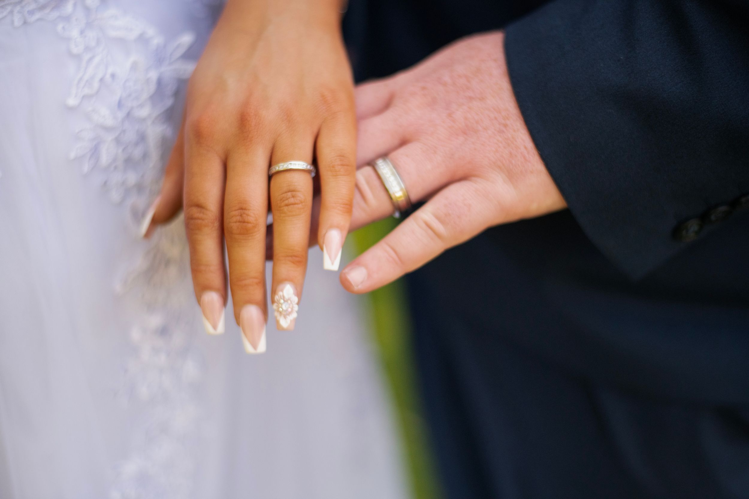 Close-up of wedding rings and manicured hands against white wedding attire.