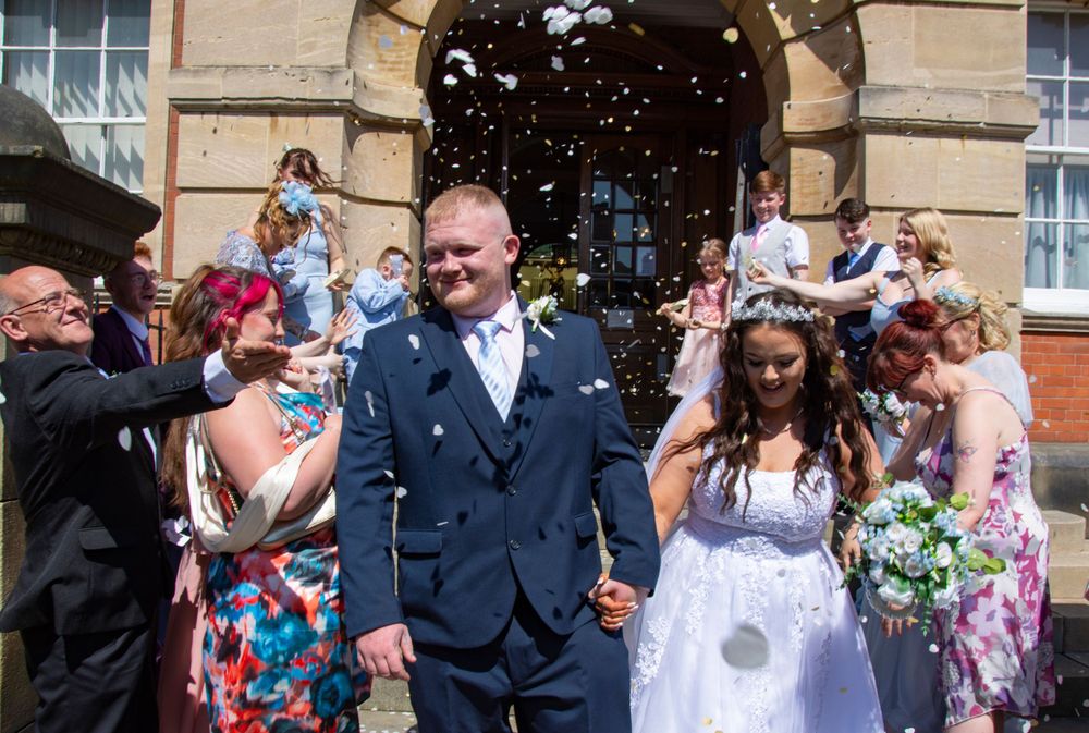 Wedding party celebrates with confetti outside historic stone building.