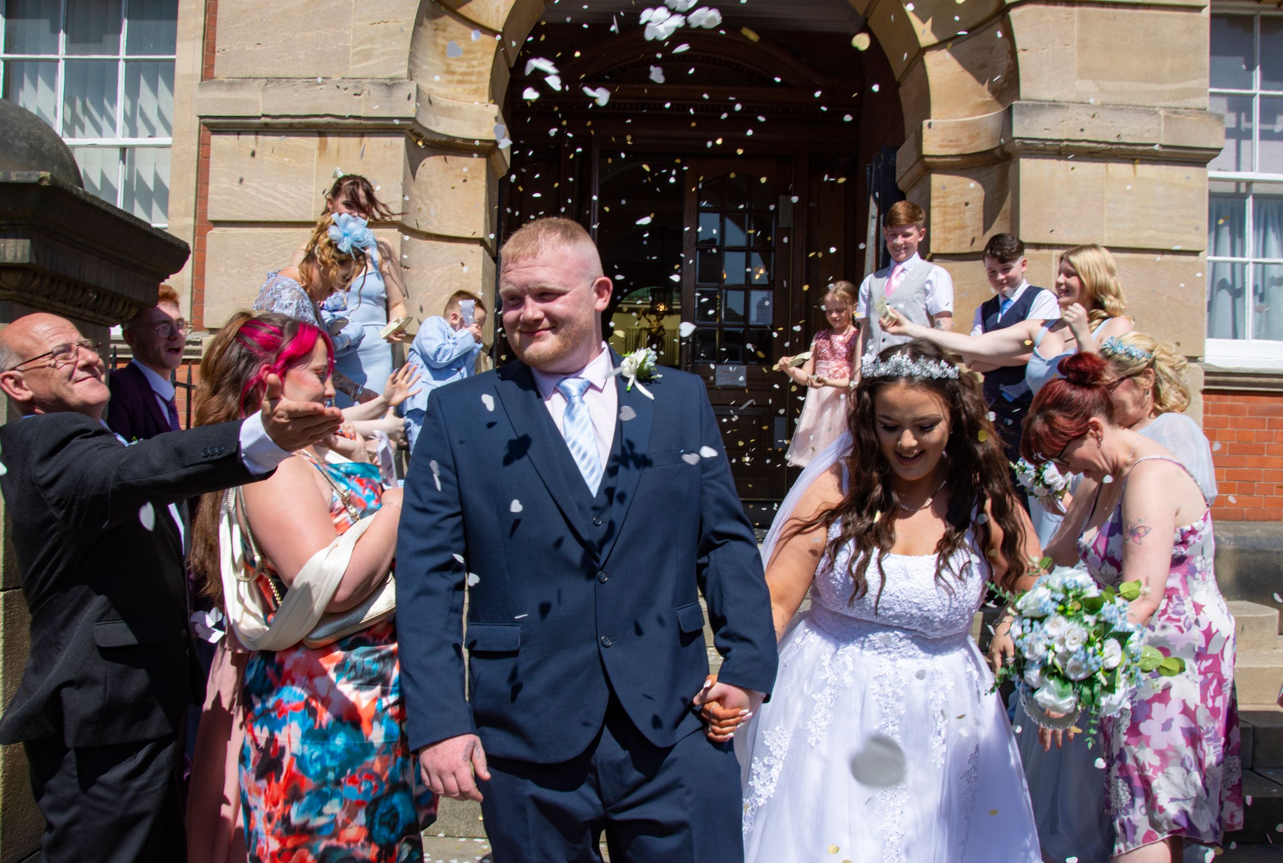 Wedding party celebrates with confetti outside historic stone building.