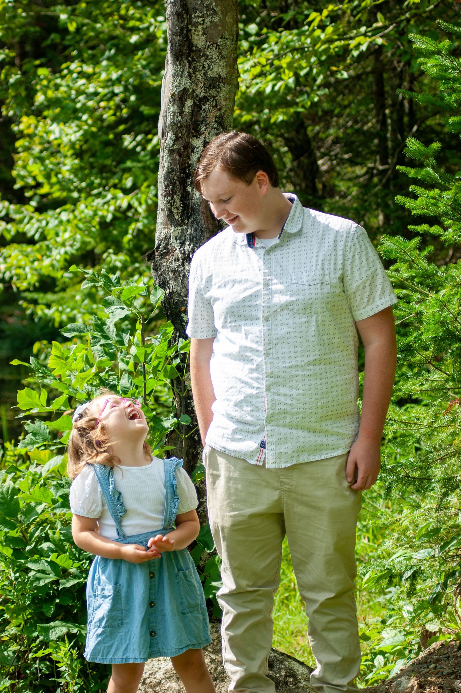 Two people share a joyful moment while standing near a tree in a lush forest setting.