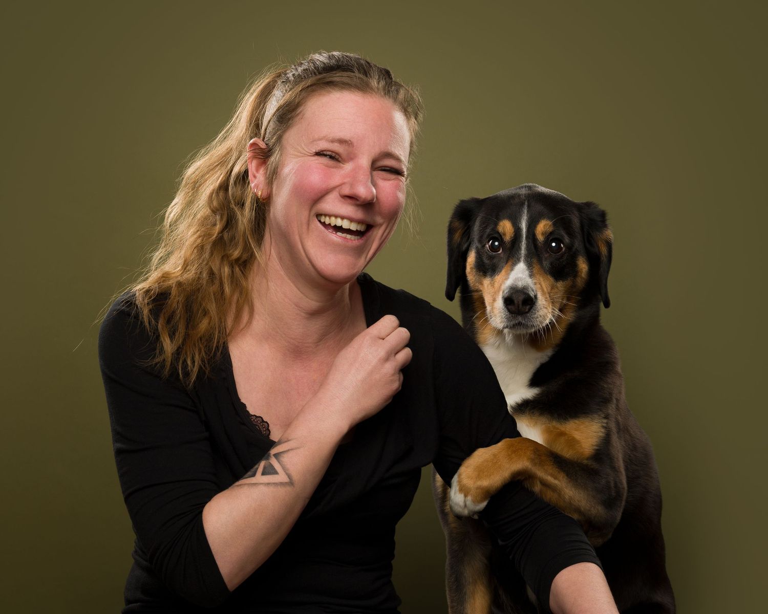 A joyful portrait of companionship between a person and their tricolor mixed breed dog against a dark background.