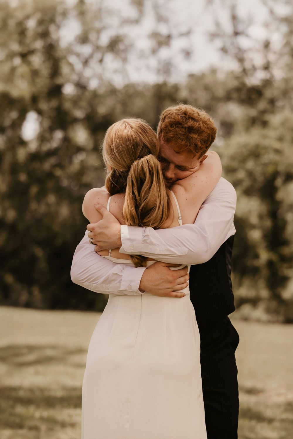 A romantic wedding couple embraces in a tender moment outdoors with a soft, warm sepia-toned filter.