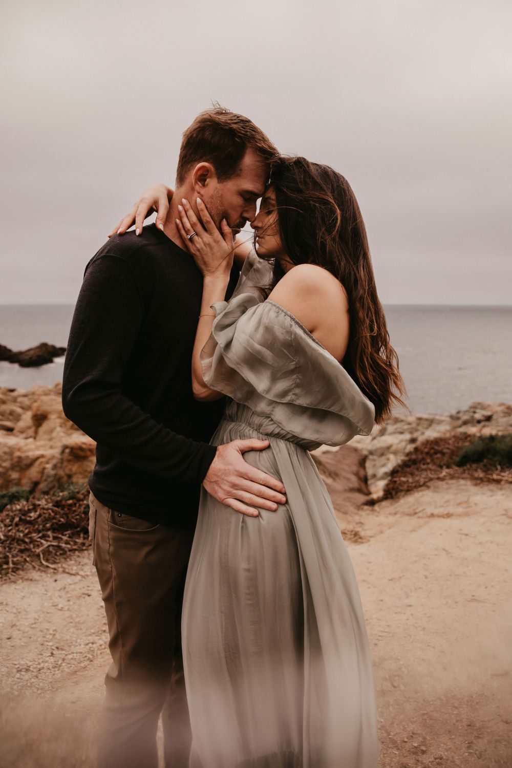 Intimate moment between couple in casual wear sharing tender embrace on coastal overlook.