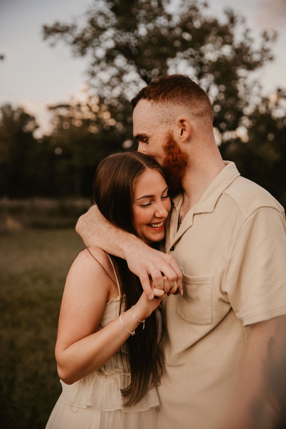 A romantic sunset portrait of a couple embracing and laughing together in a warm-toned outdoor setting.