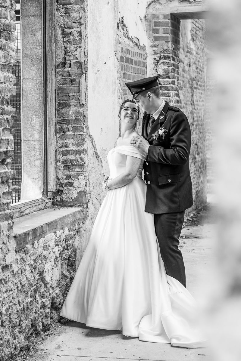 Romantic black and white portrait of a military wedding couple against a rustic brick wall.