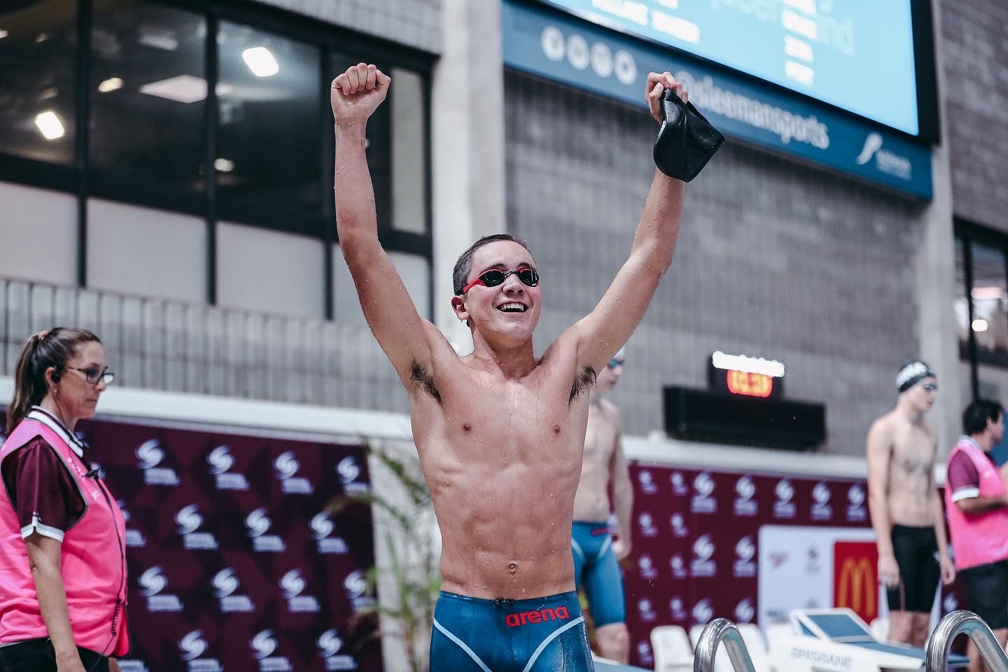 Athlete celebrates victory with raised arms and shirtless celebration in stadium setting.