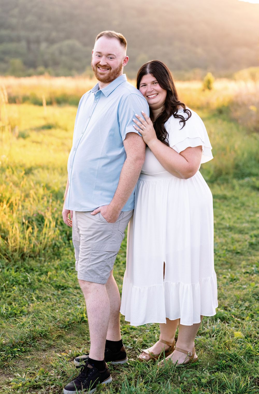 A couple embraces in a sunlit meadow wearing coordinating white and light blue outfits.
