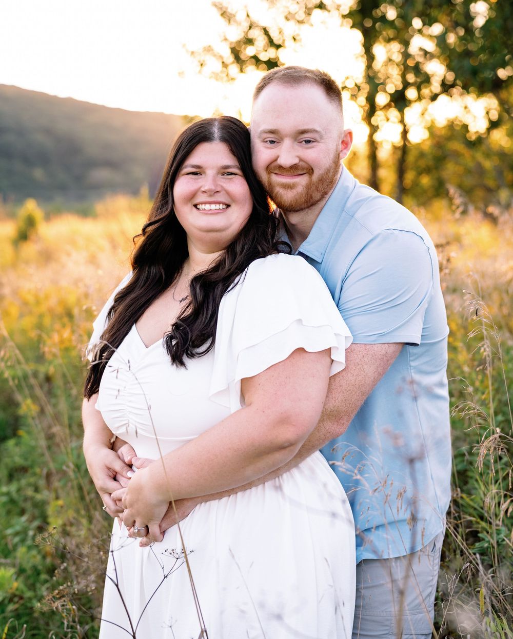 A loving couple shares joyful moments during their sunset engagement session in a meadow.