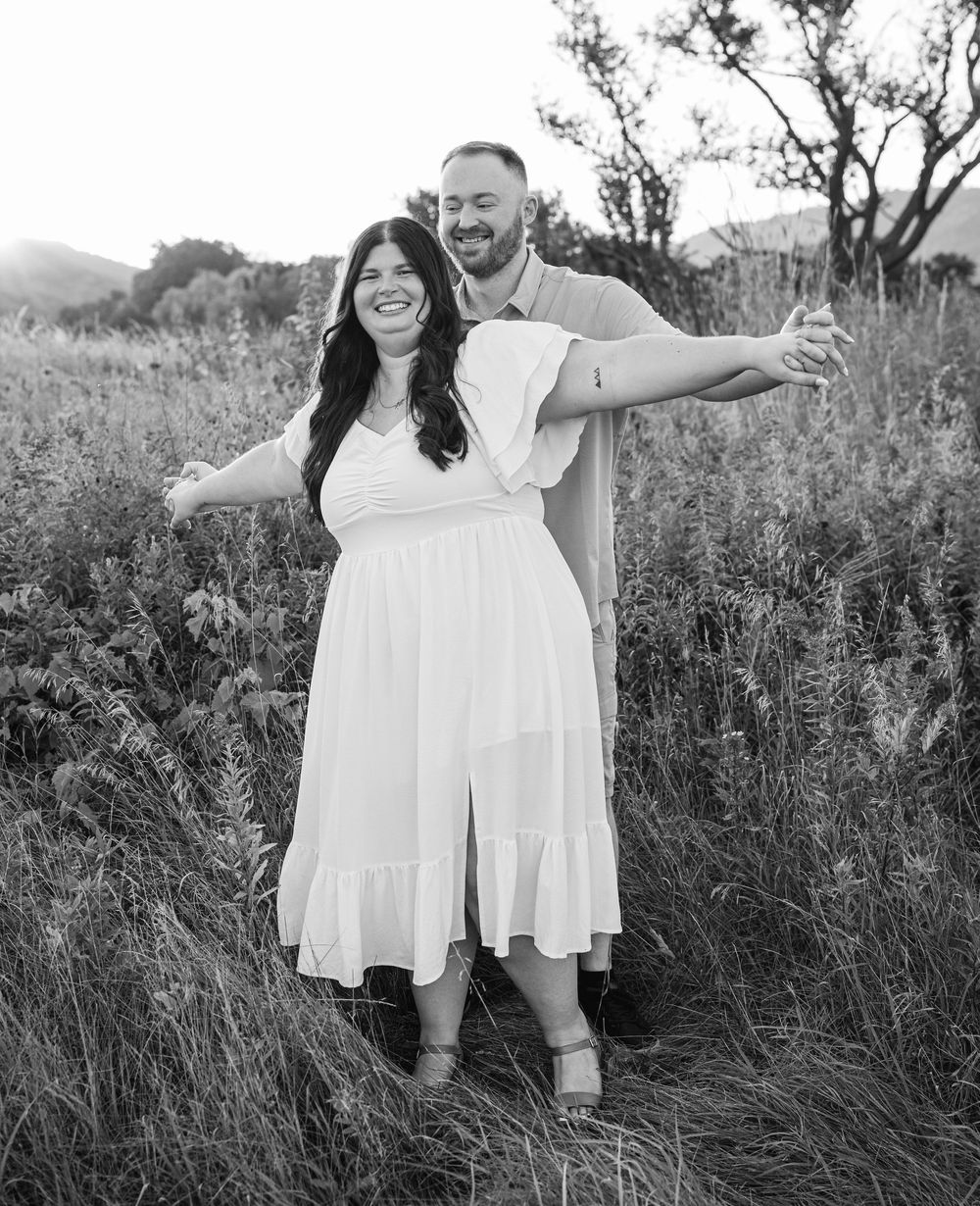 A black and white portrait of a couple laughing together in a wildflower field.