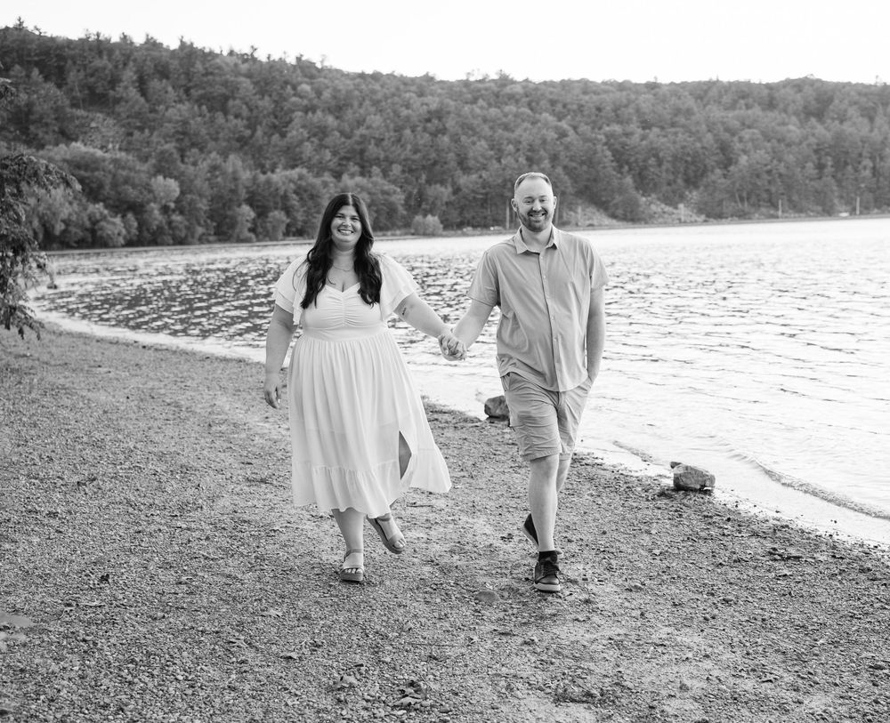 A couple walks hand in hand along a rocky beach in black and white.