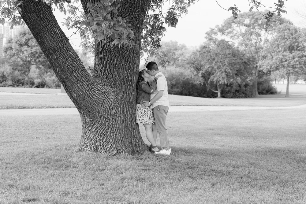 A couple sits beneath a large tree in a peaceful black and white landscape.