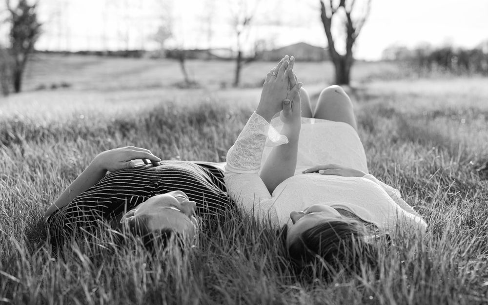 Black and white photo of a couple lying in grass, relaxing outdoors on a sunny day in a peaceful field.