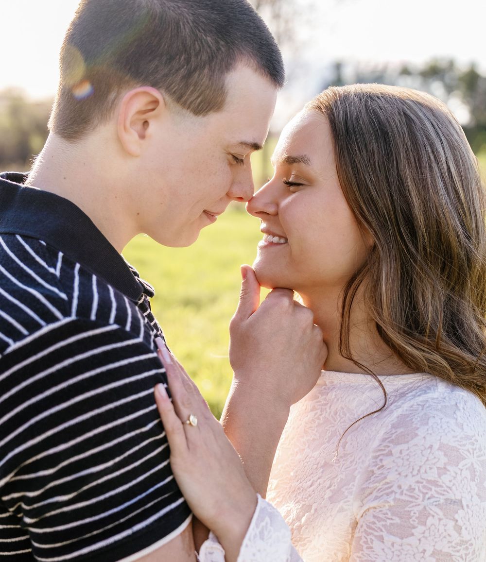 Romantic couple sharing an intimate moment outdoors, smiling and touching noses in a sunny field.