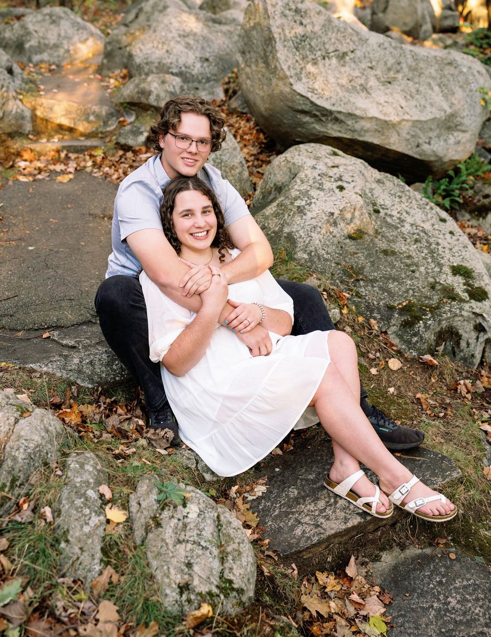 Romantic couple poses on rocky terrain surrounded by fallen autumn leaves.