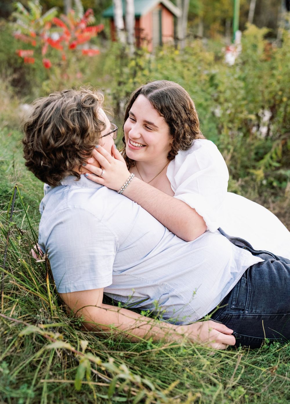 A couple shares intimate moments while lying in tall grass during a romantic outdoor photoshoot.
