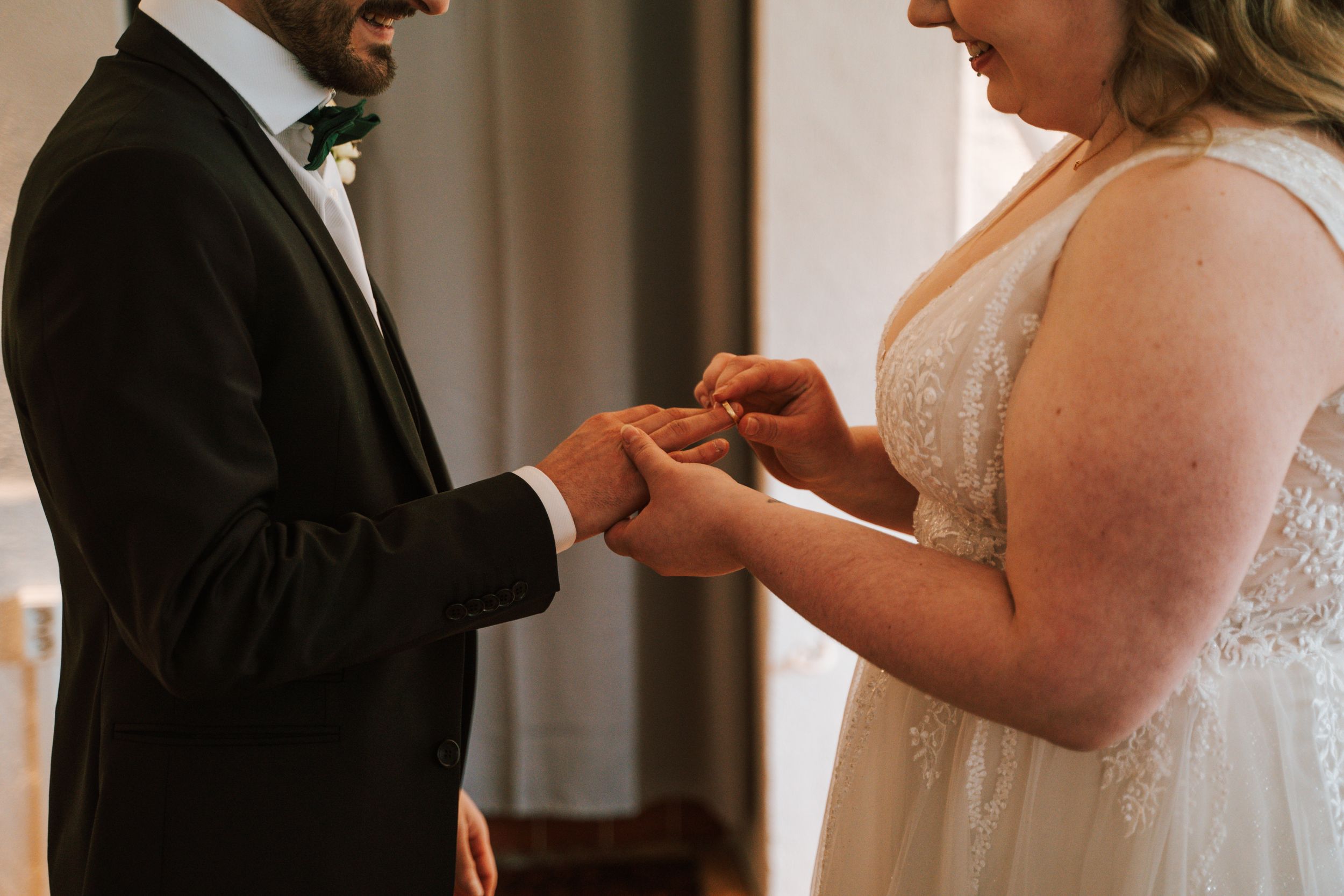 Tender moment during ring exchange at indoor wedding ceremony.