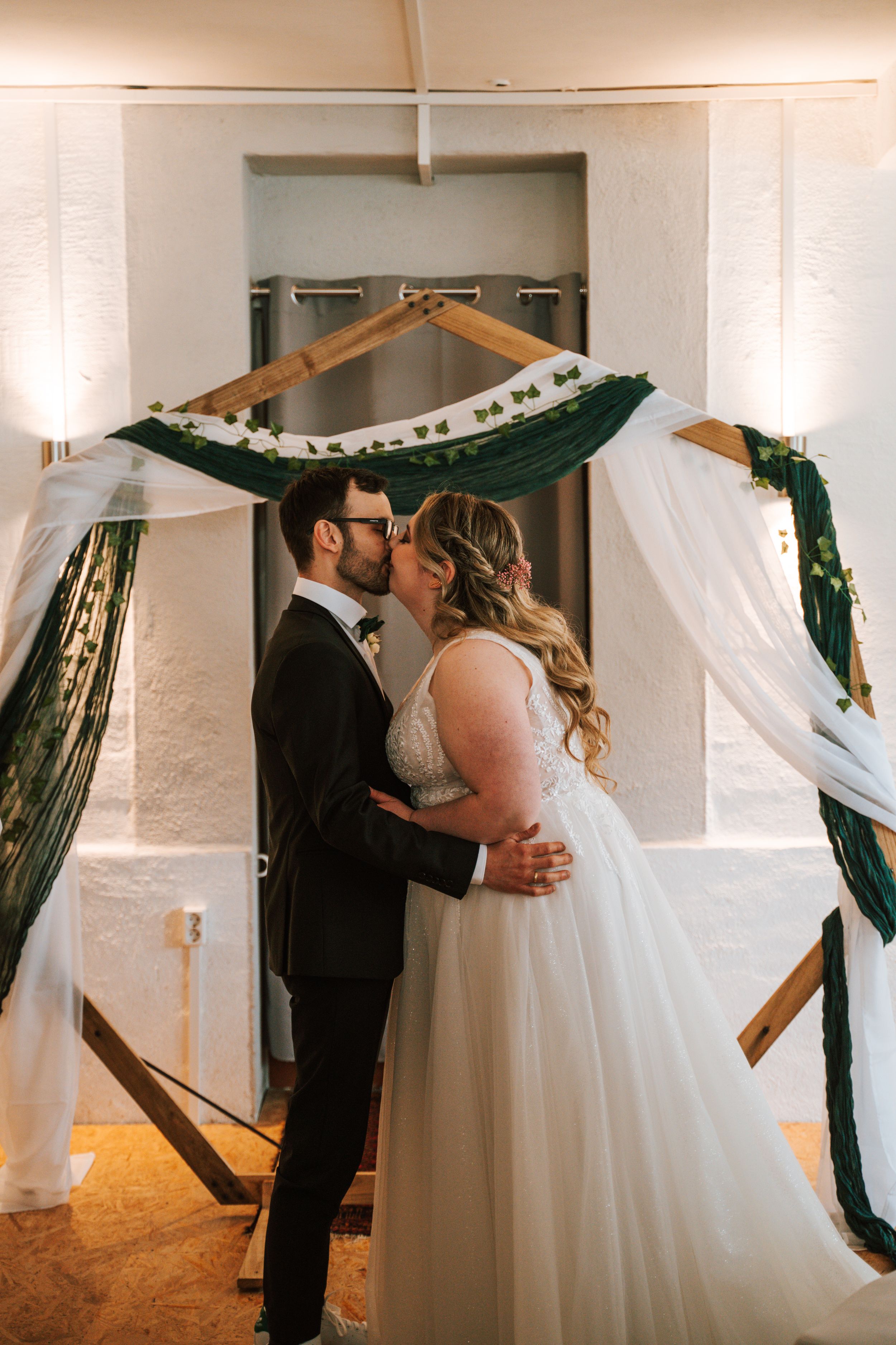 Wedding ceremony in white room with green and gold decorative backdrop.